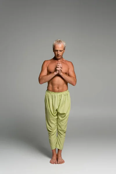 Full length of barefoot man in pants meditating while doing kali mudra on grey — Stock Photo
