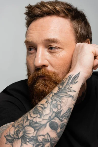 Portrait of thoughtful bearded man holding tattooed hand near face and looking away isolated on grey — Stock Photo