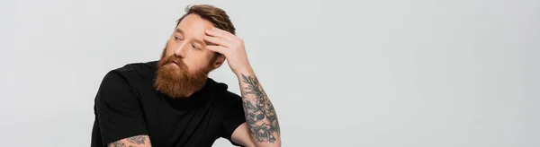 Pensive bearded man in black t-shirt touching forehead and looking away isolated on grey, banner — Stock Photo