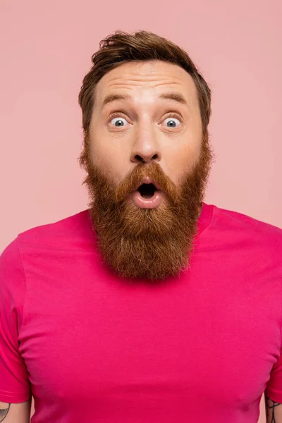 Изумленный бородатый мужчина с открытым ртом смотрит на камеру, изолированную на розовый — стоковое фото
