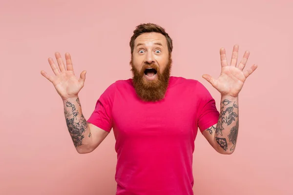 Thrilled tattooed man with open mouth showing wow gesture and looking at camera isolated on pink — Photo de stock