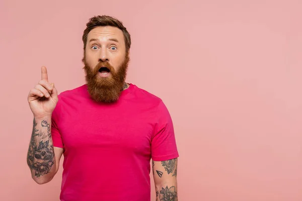 Astonished tattooed man showing idea gesture while standing with open mouth isolated on pink — Stock Photo