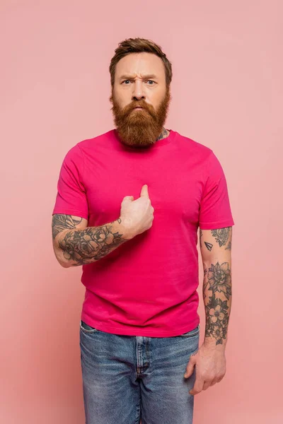 Displeased bearded man in trendy t-shirt pointing with finger at himself isolated on pink — Photo de stock