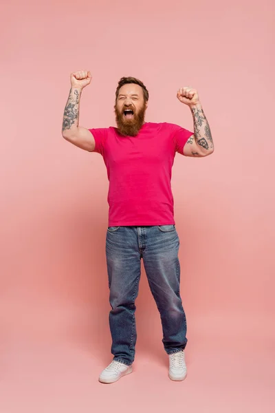 Homme à la mode en t-shirt et jeans magenta se réjouissant et criant sur fond rose — Photo de stock