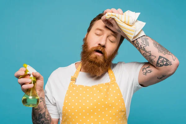 Erschöpfter bärtiger Mann mit Sprühflasche und Lappen an der Stirn — Stockfoto