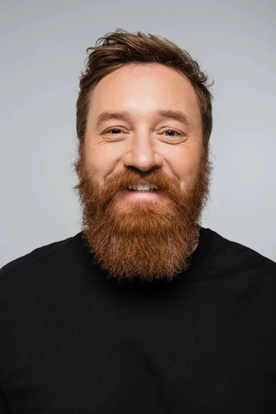 Портрет радостного человека с бородой, улыбающегося в камеру, изолированную на сером — стоковое фото
