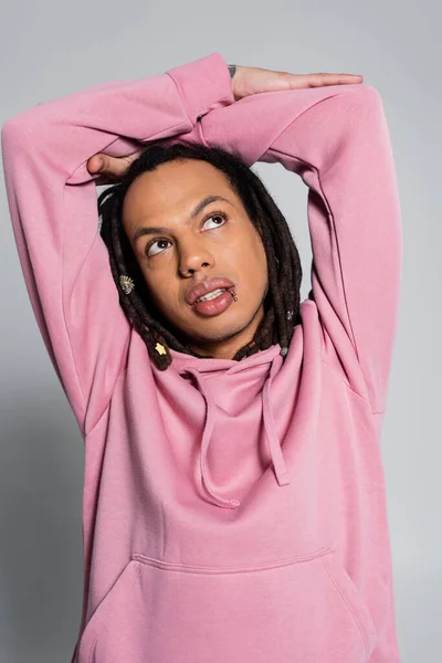 Tattooed multiracial man in pink hoodie looking up while thinking on grey — Stock Photo