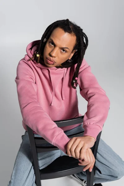 Overhead view of multiracial man with dreadlocks sitting on chair and looking at camera isolated on grey — Stock Photo