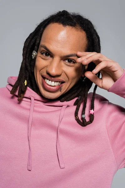 Portrait of happy multiracial man in pink hoodie looking at camera isolated on grey - foto de stock