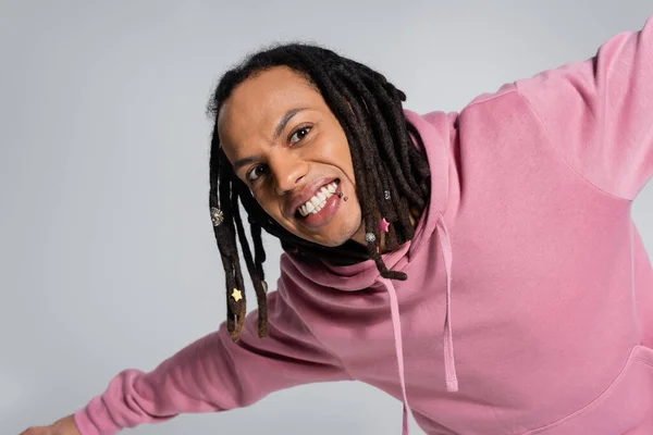 Portrait of smiling multiracial man in pink hoodie looking at camera isolated on grey — Stockfoto