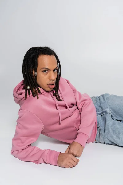 Multiracial and pierced man with dreadlocks looking at camera and sitting on grey — Stock Photo