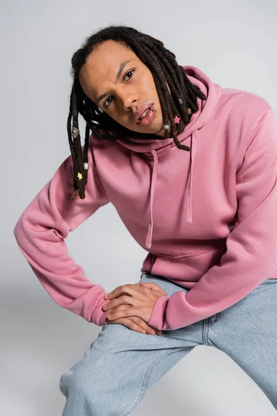 Багаторасовий чоловік в джинсах і рожевий светр дивиться на камеру, позує на сірий — стокове фото