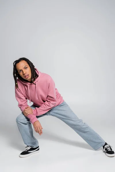 Full length of multiracial and pierced man with dreadlocks posing while looking at camera on grey — Stock Photo