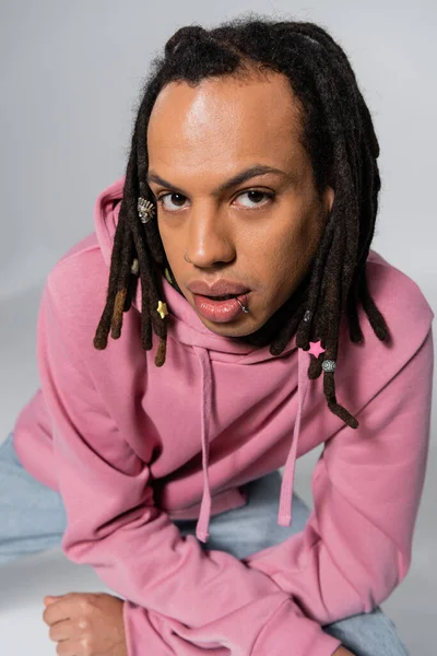 Overhead view of multiracial and pierced man with dreadlocks looking at camera on grey — Stock Photo