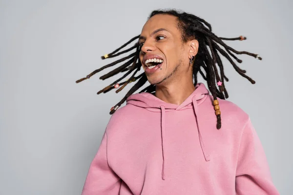 Positive multiracial man with dreadlocks shaking head and smiling isolated on grey — Stockfoto