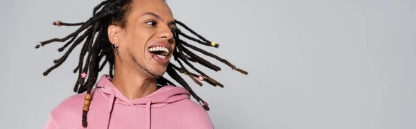 Positive multiracial man with dreadlocks shaking head and smiling isolated on grey, banner — Stockfoto