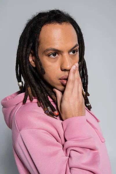 Multiracial man with dreadlocks and piercing covering mouth with hand isolated on grey - foto de stock