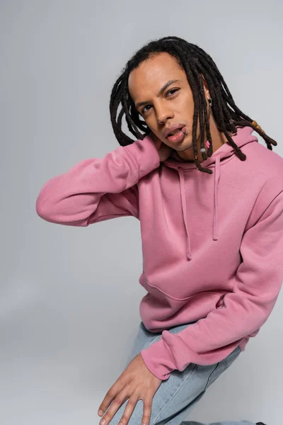 Pierced multiracial man with dreadlocks looking at camera and posing on grey — Stock Photo