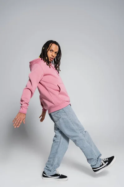Mann in blauer Jeans und rosa Kapuzenpulli posiert auf grau — Stockfoto
