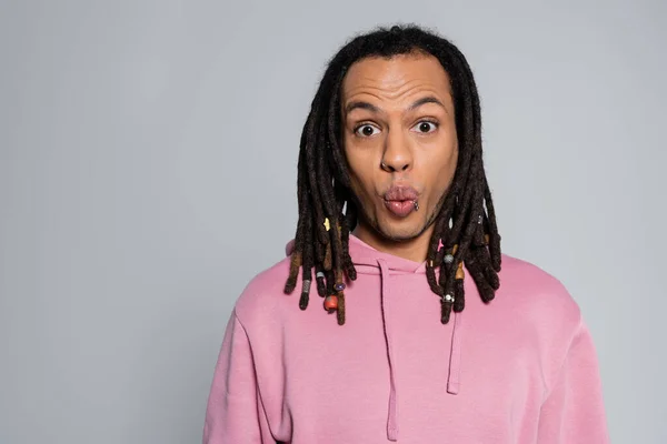 Shocked multiracial man in pink hoodie pouting lips and looking at camera isolated on gray — Stock Photo