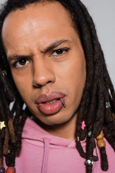 Close up of pensive multiracial man in pink hoodie looking at camera isolated on gray — Stock Photo