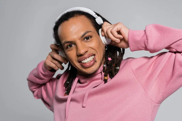 Happy multiracial man with dreadlocks listening music in wireless headphones isolated on grey — Stock Photo