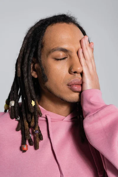 Portrait of pierced multiracial man covering closed eye isolated on grey — Stock Photo