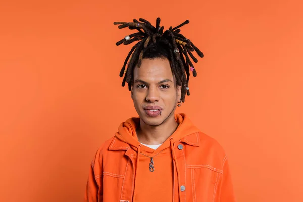 Portrait of pierced multiracial man with dreadlocks looking at camera isolated on coral background — Stockfoto