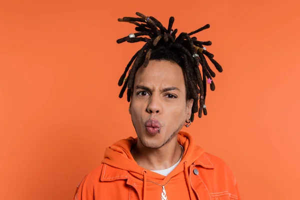 Portrait of pierced multiracial man with dreadlocks pouting lips isolated on coral background - foto de stock
