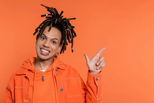 Happy multiracial man with dreadlocks pointing with finger isolated on coral background — Foto stock