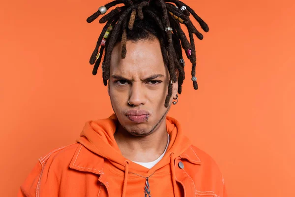 Triste homem multirracial com dreadlocks bebendo lábios isolados em fundo de coral — Fotografia de Stock