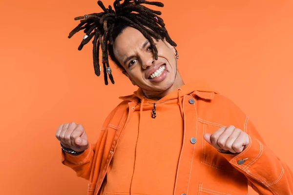 Excited and multiracial man with dreadlocks looking at camera while standing with clenched fists isolated on coral background — Stock Photo