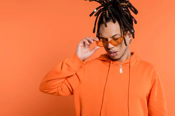 Multiracial man with dreadlocks wearing stylish sunglasses isolated on coral — Stock Photo