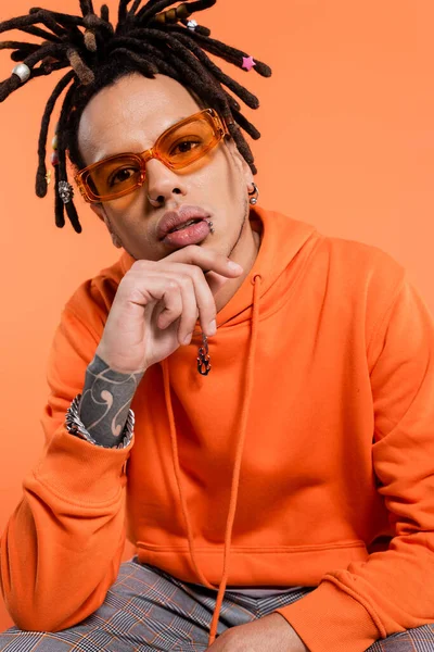 Tattooed multiracial man with dreadlocks and stylish sunglasses isolated on coral — Stock Photo