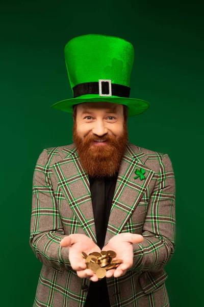 Улыбающийся бородатый мужчина в шляпе держит монеты, празднуя день святого Патрика, изолированного на зеленом — стоковое фото