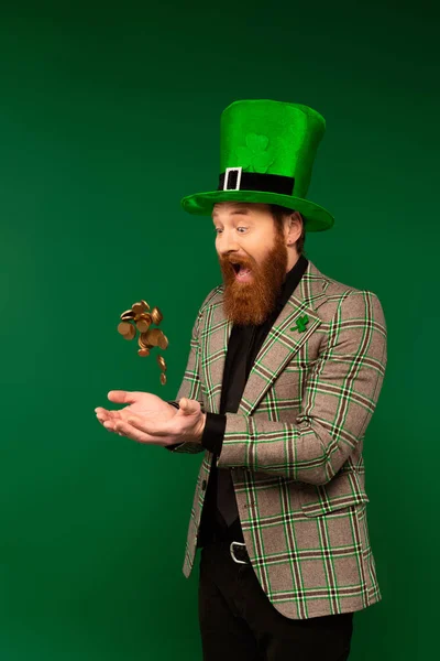 Shocked bearded man in hat throwing coins during saint patrick day isolated on green — Fotografia de Stock