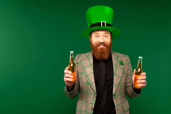 Smiling bearded man in hat holding bottles of beer isolated on green - foto de stock