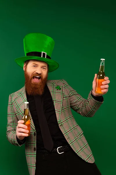 Homme excité en veste et chapeau tenant des bouteilles de bière isolées sur vert — Photo de stock