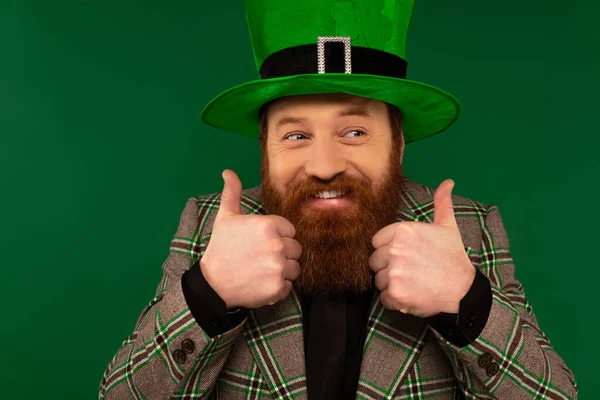 Sonriente hombre barbudo con sombrero mostrando como gesto aislado en verde - foto de stock