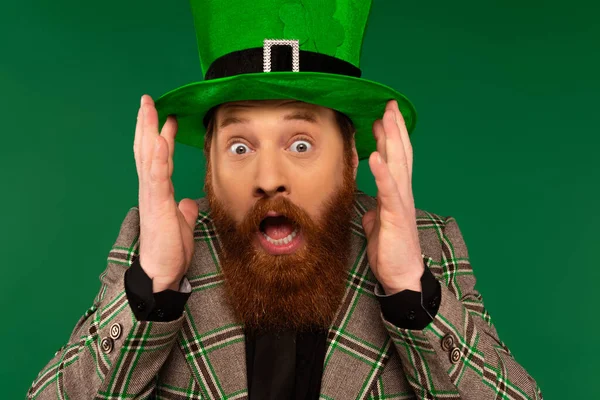 Scared bearded man in hat with clover looking at camera isolated on green — Foto stock