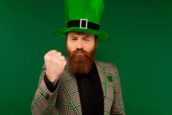 Uomo barbuto arrabbiato in cappello con trifoglio mostrando pugno isolato sul verde — Foto stock
