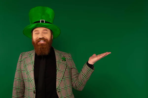 Allegro uomo in cappello con trifoglio che punta con mano isolata sul verde — Foto stock