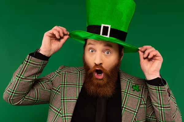 Shocked bearded man wearing hat with clover isolated on green - foto de stock