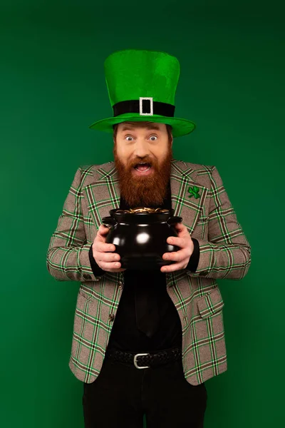 Bearded man in hat with clover holding pot with golden coins isolated on green — Fotografia de Stock