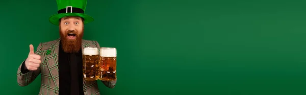 Homme étonné en chapeau tenant de la bière et montrant pouce vers le haut isolé sur vert, bannière — Photo de stock