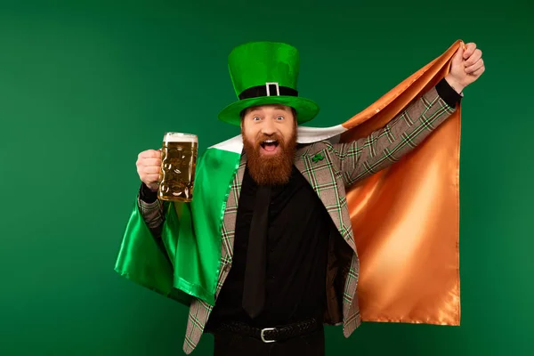 Excited man in hat holding glass of beer and Irish flag isolated on green — Photo de stock