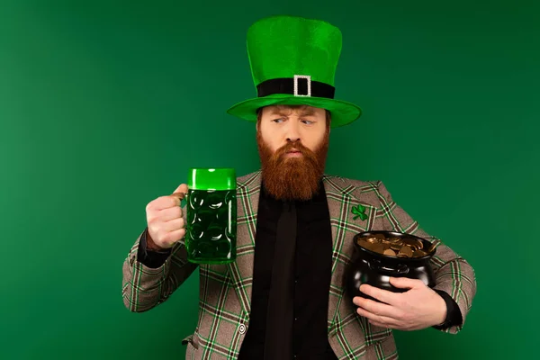 Людина в капелюсі тримає келих пива і горщика з золотими монетами ізольовані на зеленому — стокове фото