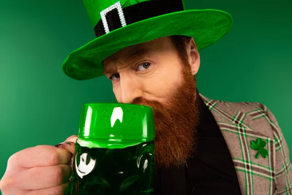 Retrato de hombre barbudo en sombrero bebiendo cerveza y mirando a la cámara aislada en verde - foto de stock