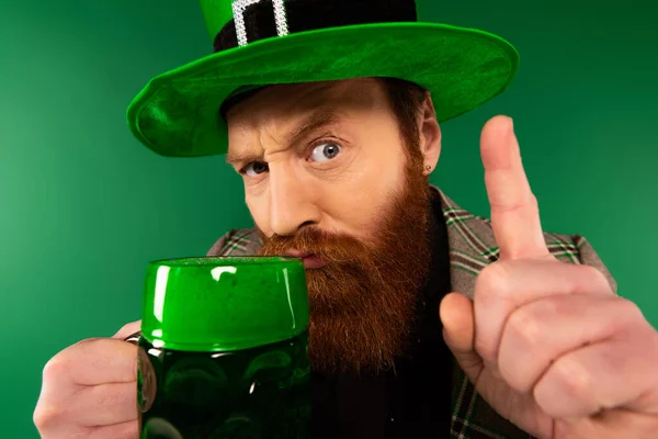 Серьезный человек в шляпе имея идею и держа стакан пива изолированы на зеленый — стоковое фото