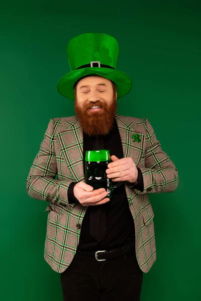 Homem barbudo alegre segurando um copo de cerveja enquanto celebra o dia de São Patrício isolado no verde — Fotografia de Stock